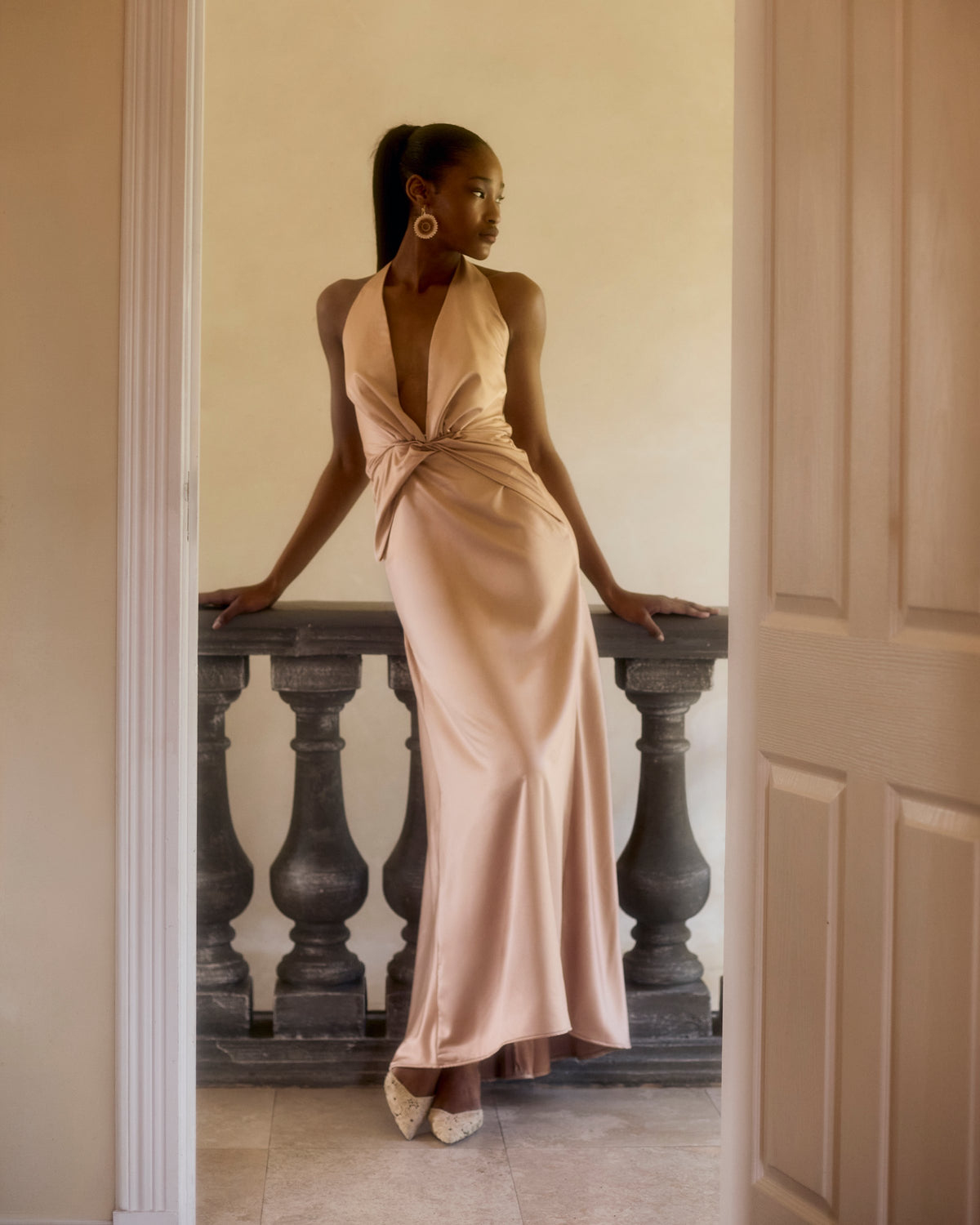 Idai Dress in soft pink satin, standing in a doorway