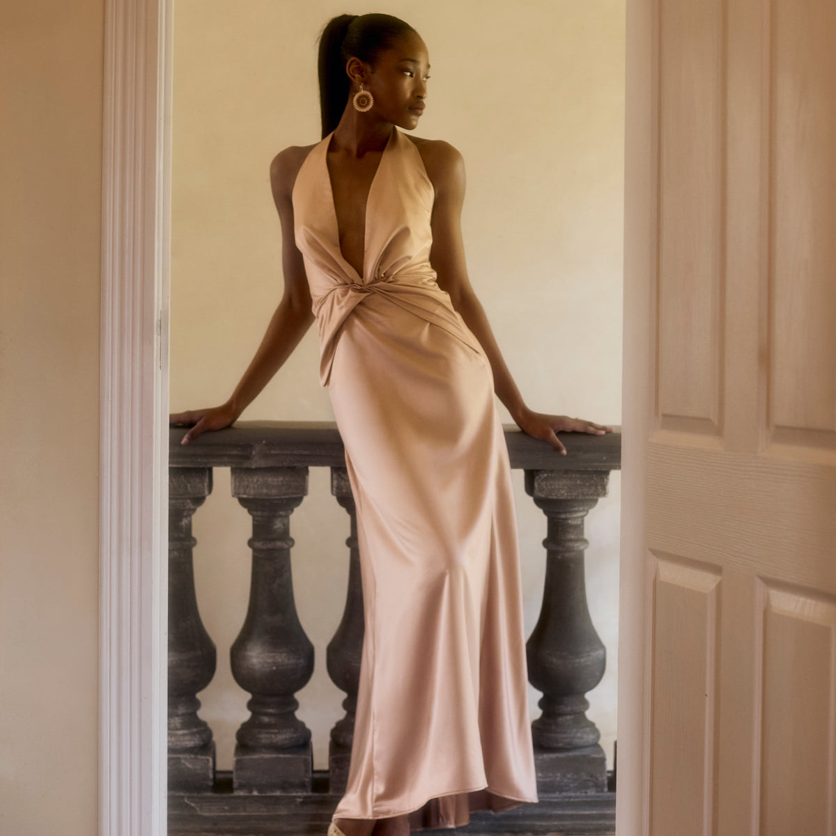 Idai Dress in soft pink satin, standing in a doorway